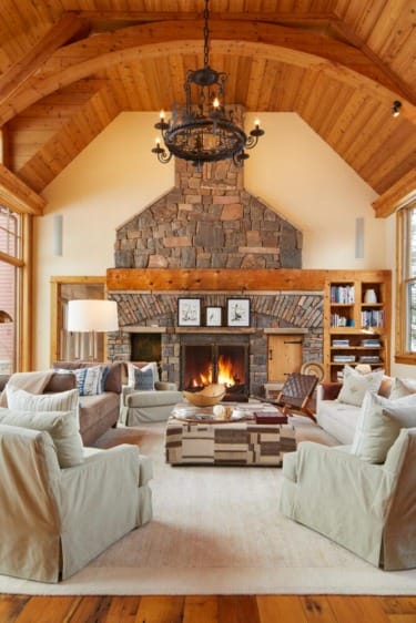 Cozy living room with stone fireplace, chandelier, and wooden ceiling, surrounded by comfy chairs and sofas.