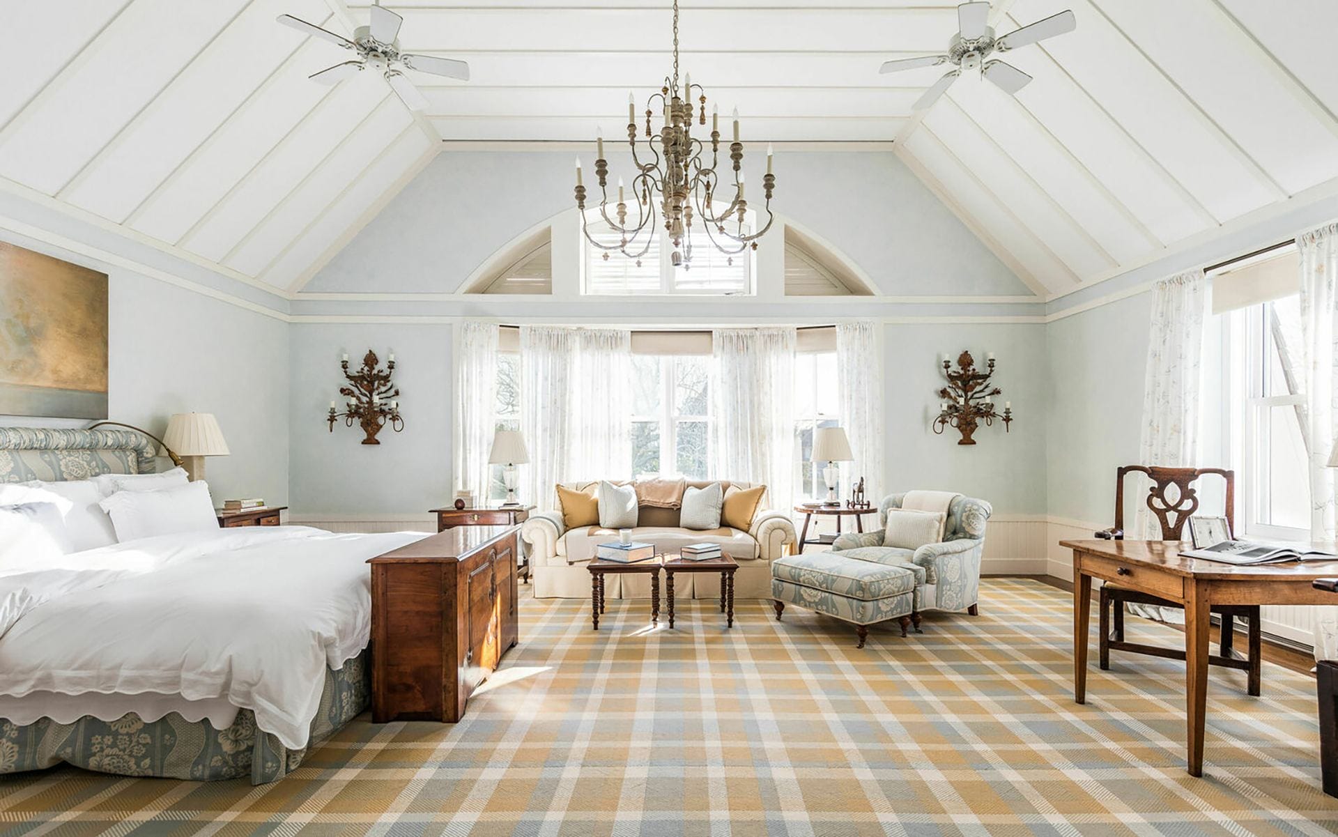 Luxurious bedroom with a large bed, elegant chandelier, plaid carpet, cozy seating area, and expansive windows.