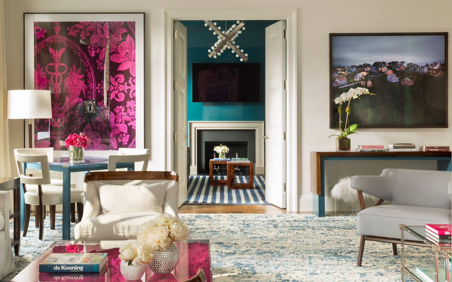 Colorful modern living room with large artworks, patterned rug, elegant furniture, and a fireplace in the background.