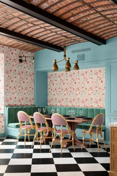 Stylish dining area with a round table, patterned chairs, floral wallpaper, green seating, and checkerboard floor.