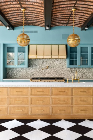 Luxurious kitchen with wooden cabinets, marble countertop, gold fixtures, geometric floor, teal walls, and brick ceiling.