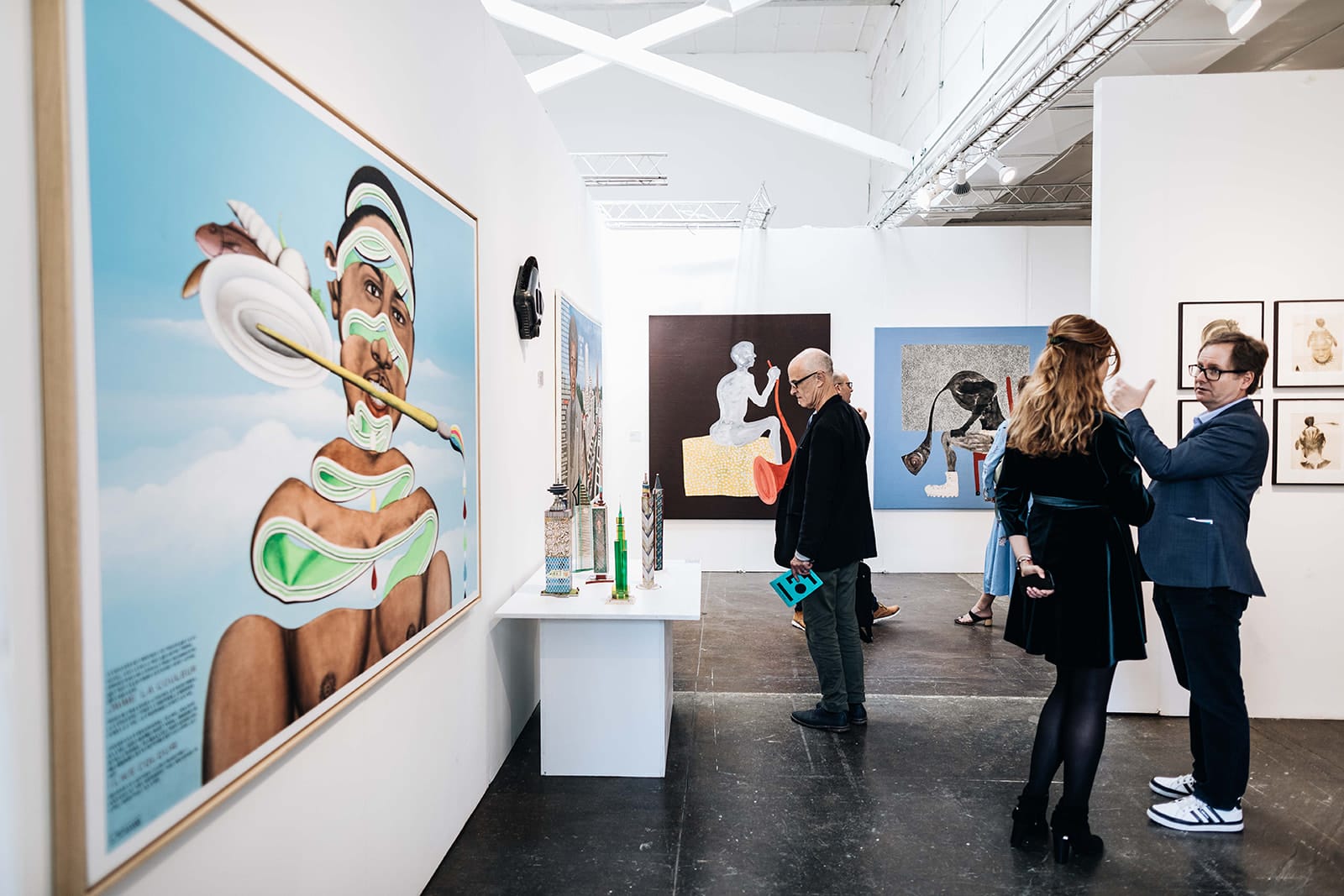 People observing modern art at a gallery exhibition, featuring diverse and vibrant paintings on white walls.