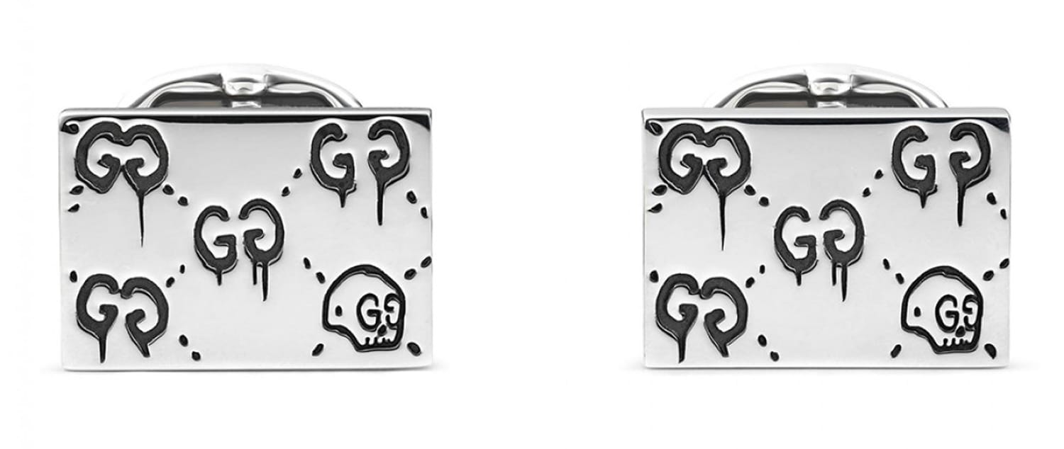 Silver rectangular cufflinks with engraved patterns of hearts, skulls, and letter G initials on the surface.