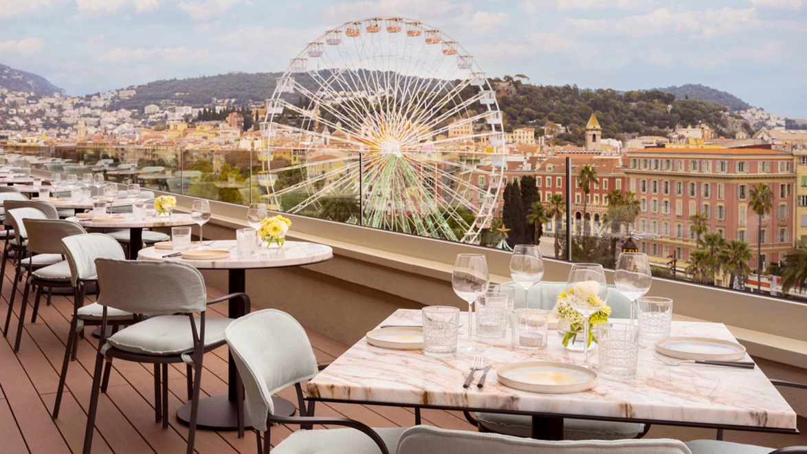 Rooftop dining area with tables set, offering a view of a Ferris wheel and cityscape in the background.