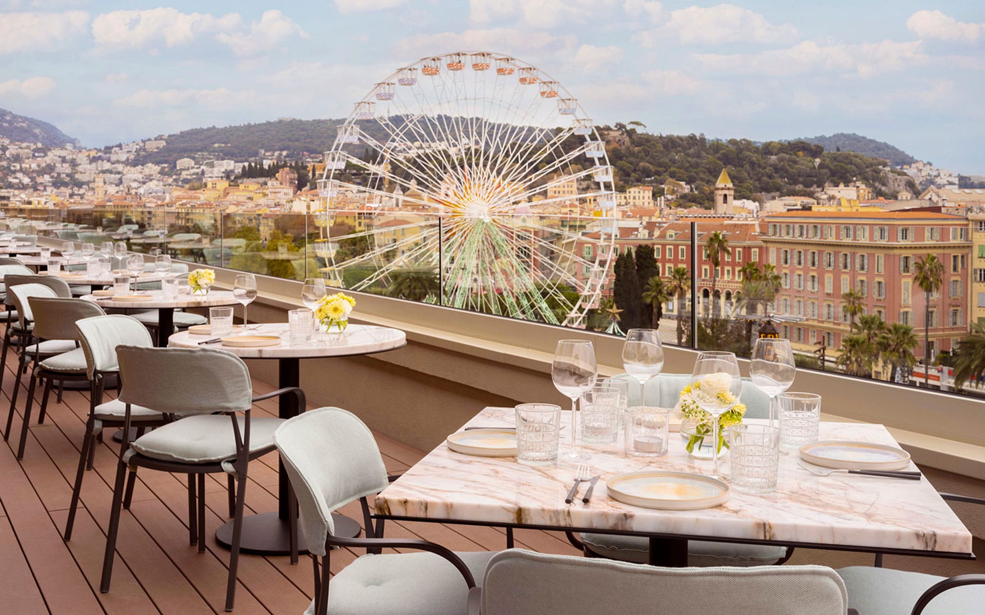 Rooftop dining area with tables set, offering a view of a Ferris wheel and cityscape in the background.