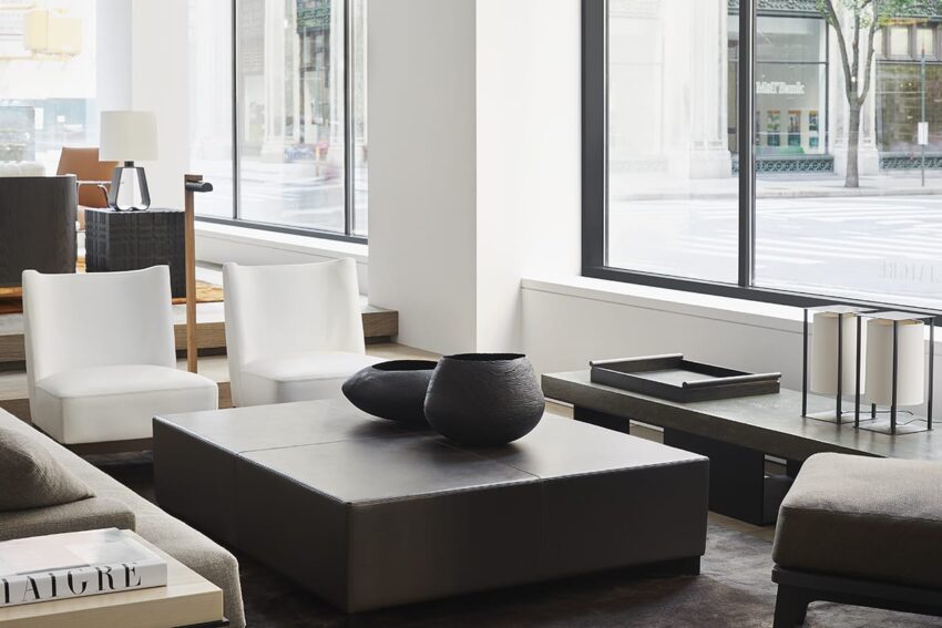 Modern living room with large windows, sleek furniture, black coffee table, white chairs, and decorative bowls.