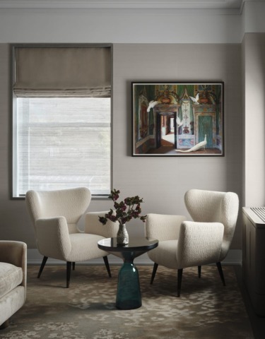Cozy living room with two white armchairs, a round table with flowers, and a framed painting on the wall.