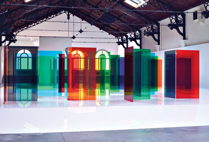 Art installation with colorful transparent panels reflecting on a glossy floor in an industrial-style gallery space