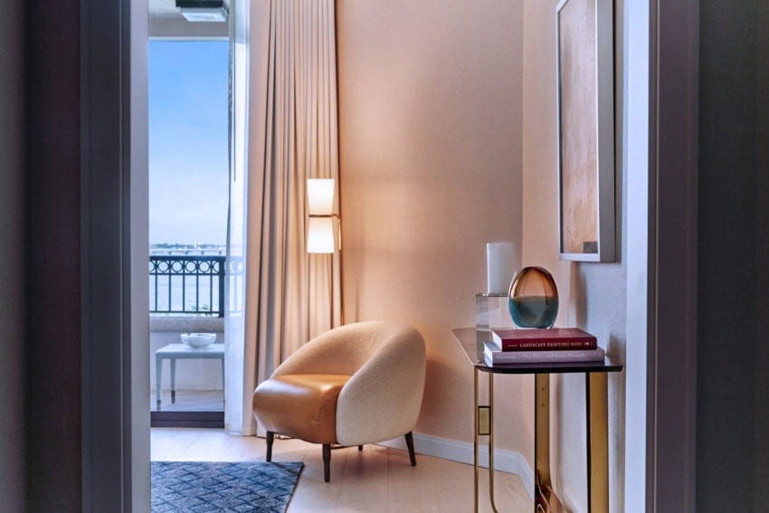 Cozy chair in elegant room with large window, soft lighting, side table with books, and a view of a balcony.