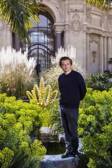 Person standing in a lush garden with a historic building in the background.
