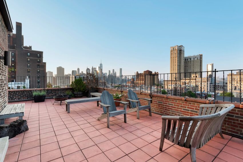 Rooftop terrace with wooden chairs and benches overlooking a city skyline on a clear day.