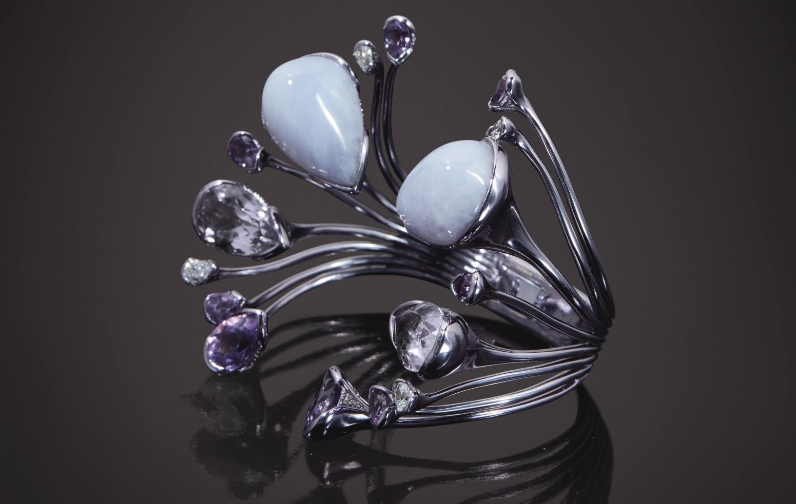 Modern, abstract silver bracelet with large pale blue stones and smaller purple and clear gems on a dark background.
