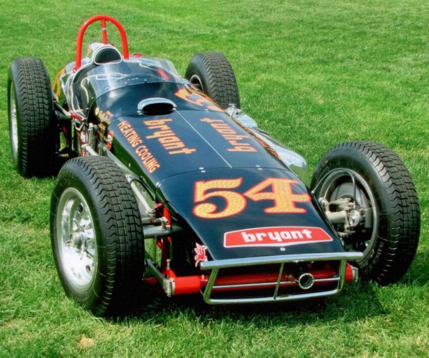 Vintage racing car, number 54, with sponsor logos, parked on grass field.