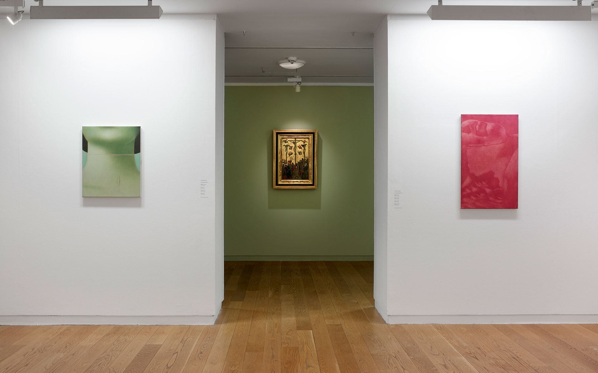 Art gallery with three paintings on display, one on each white wall and a centerpiece in a green room, wood flooring.