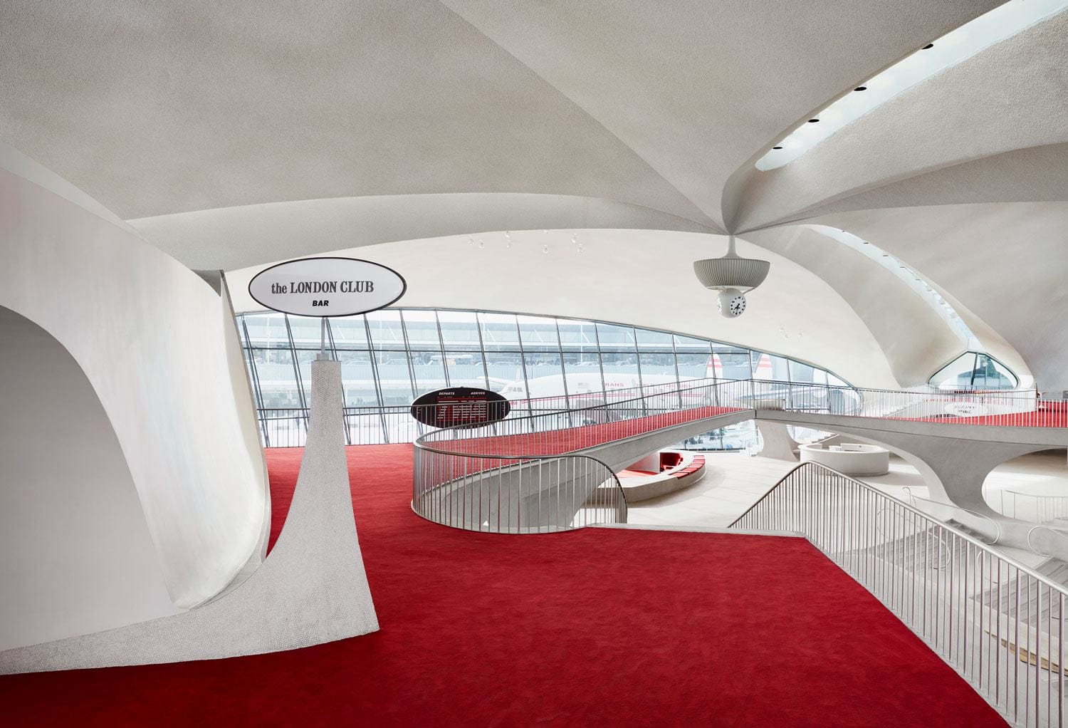 Futuristic interior of a modern building with sweeping white curves, red carpet, and large glass windows.