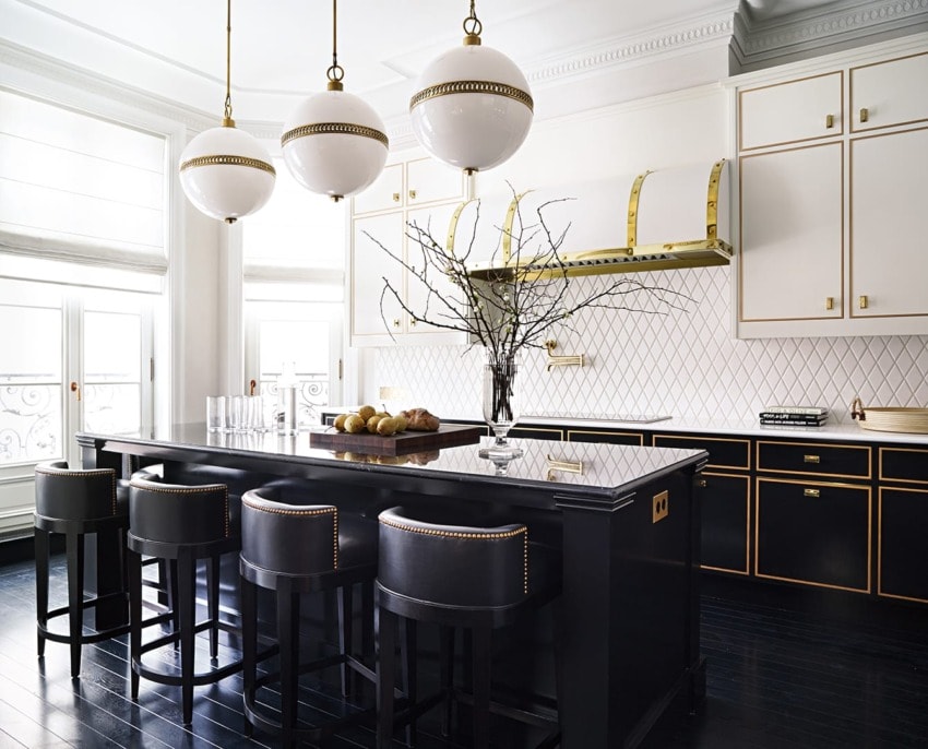 Modern kitchen with black island, white cabinets, gold accents, three pendant lights, and fruit centerpiece.