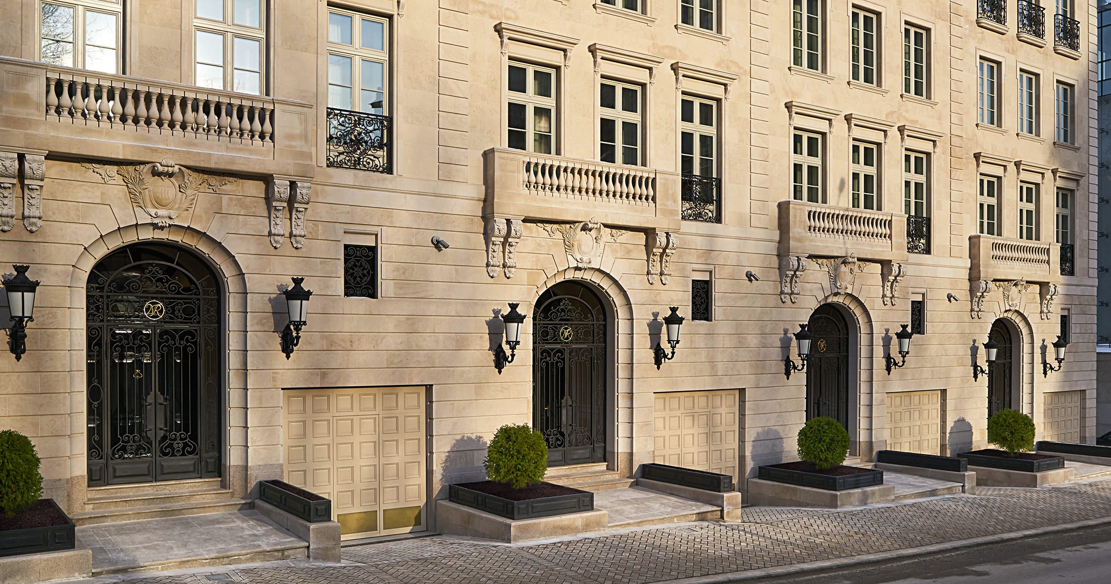Historic building facade with ornate architecture, large arched doors, decorative lanterns, and potted plants along the sidewalk.