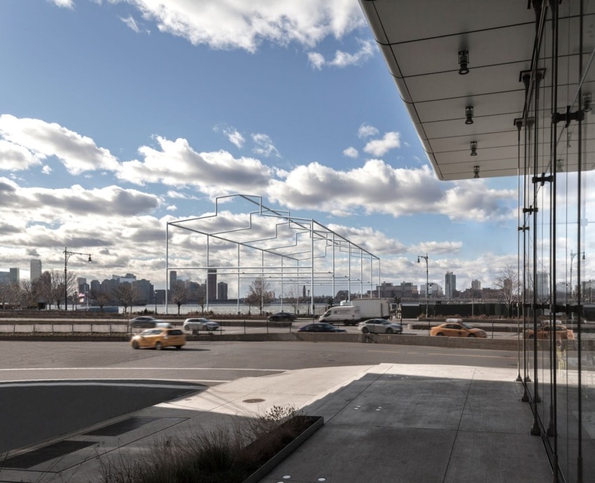 Modern building with large glass windows overlooking a road with moving traffic and a city skyline in the background.