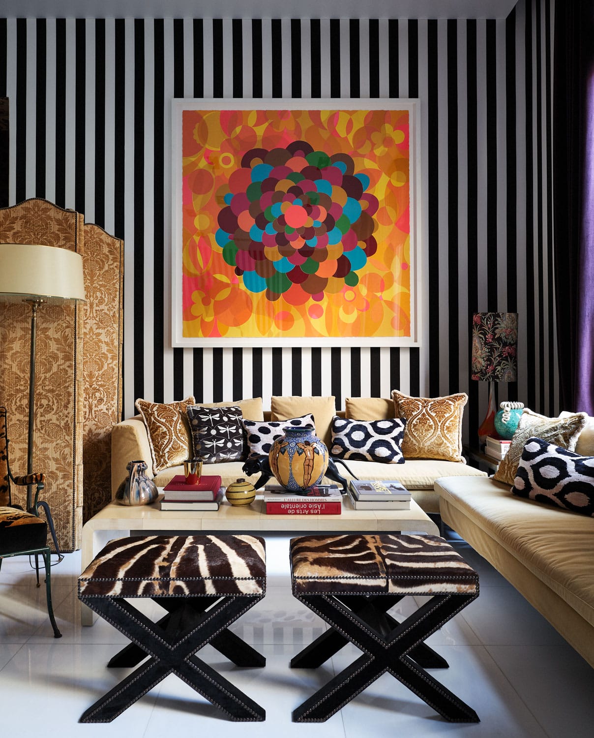 Eclectic living room with striped walls, colorful abstract art, patterned cushions, and modern furniture.