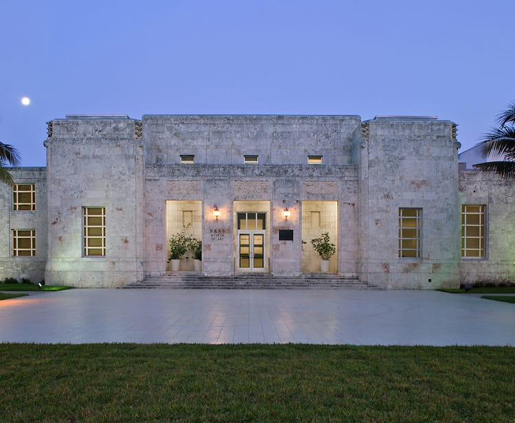 Front view of an art deco building with lit windows and entrance, set against a clear evening sky.