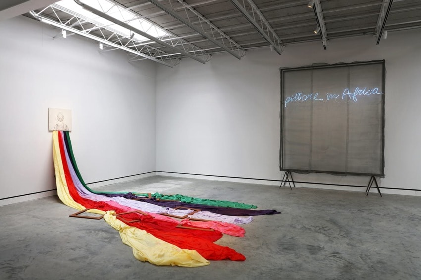 Art installation with colorful fabric flowing from a picture on the wall and a neon sign in the gallery reading "Africa".