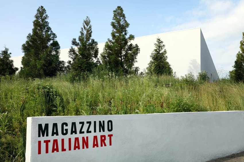 Museum building surrounded by greenery with "Magazzino Italian Art" written on a white wall in the foreground.