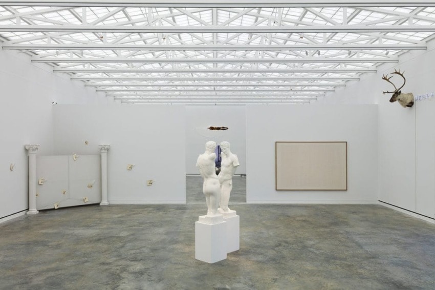 Modern art gallery interior with sculptures, abstract artwork on walls, and deer antlers mounted on right side.