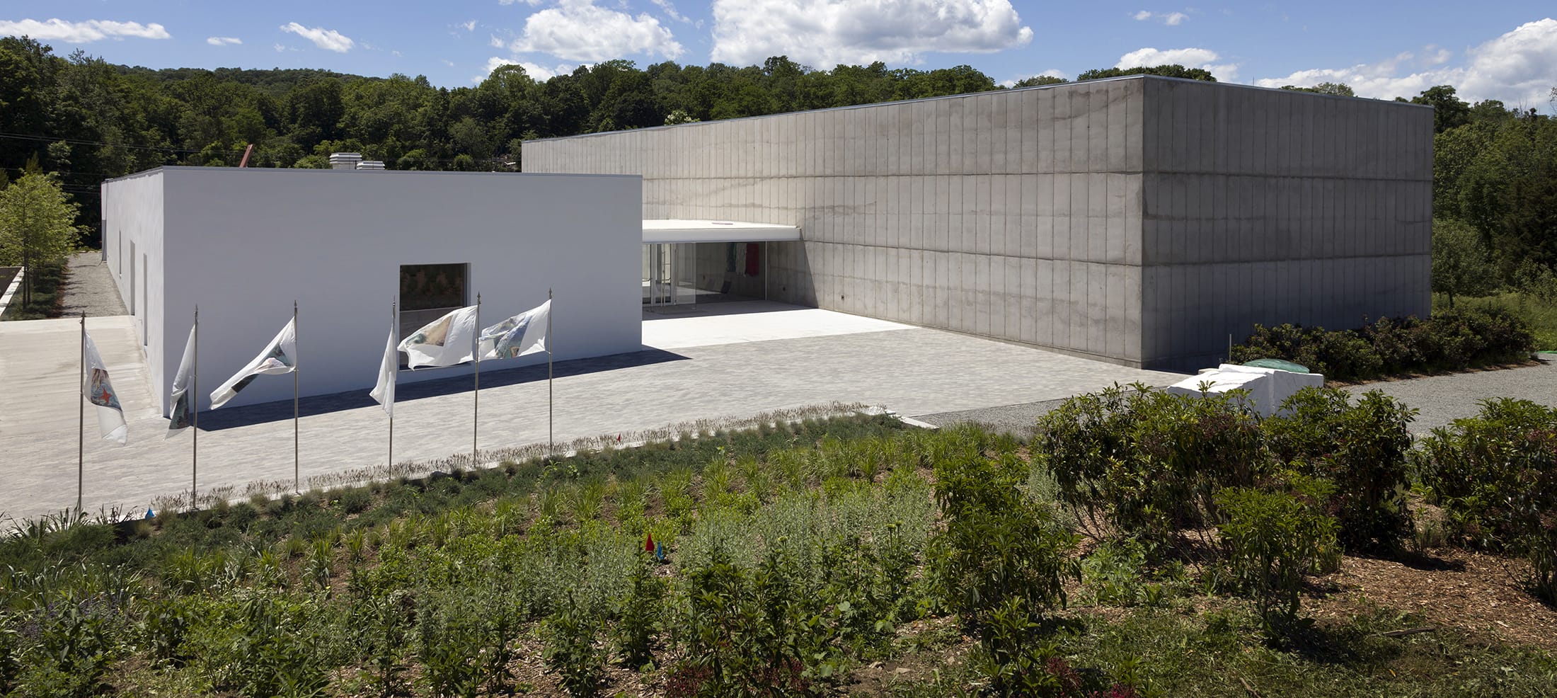 Modern art museum with a minimalist design, lush greenery in foreground, and a clear blue sky in the background.