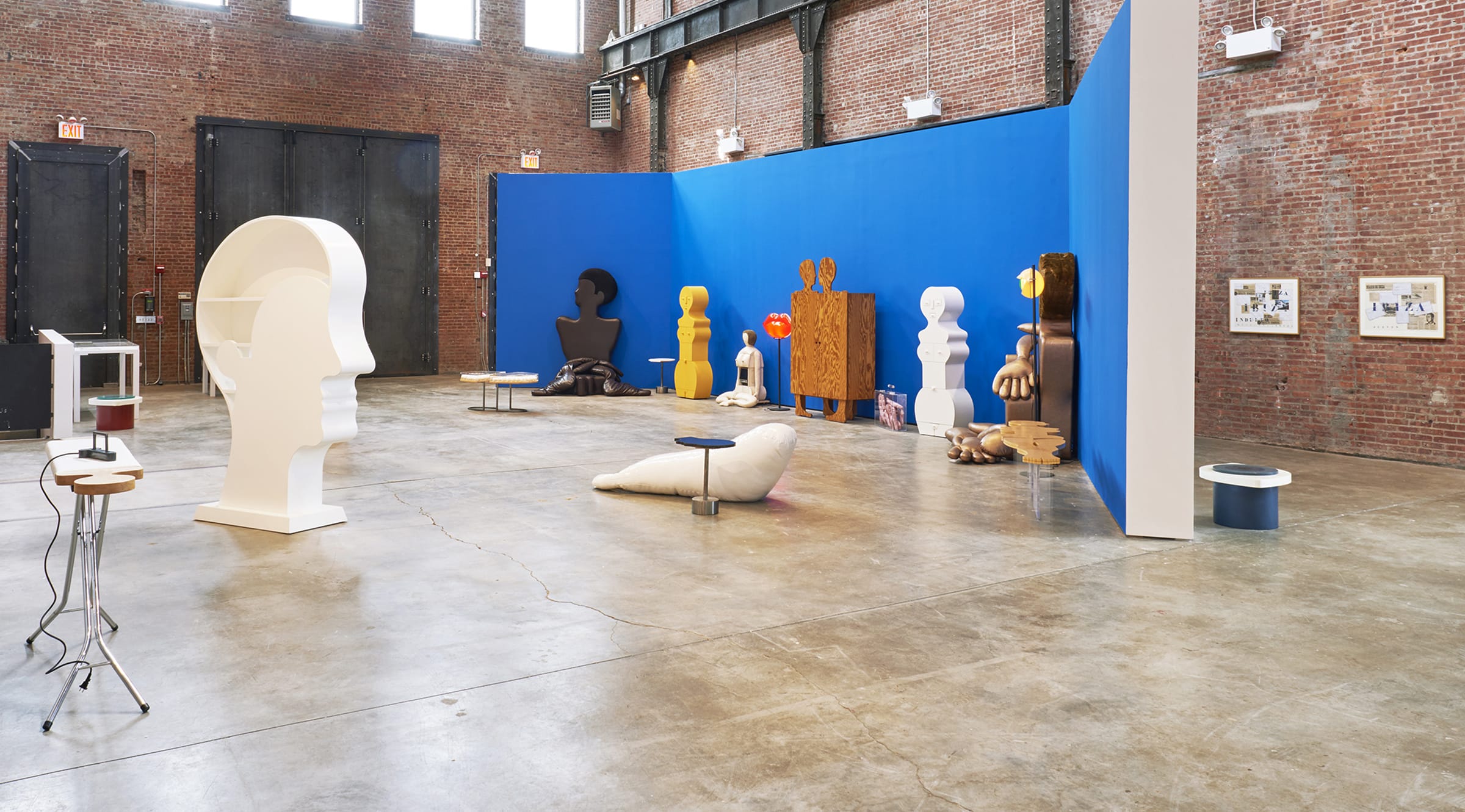 Art installation in spacious gallery with diverse abstract sculptures and vibrant blue wall backdrop.