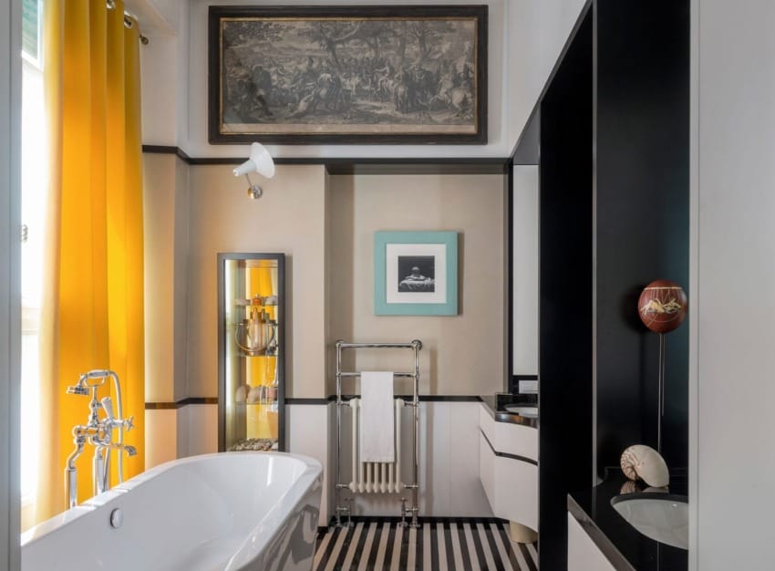 Modern bathroom with freestanding tub, yellow curtains, striped floor, and art on walls.