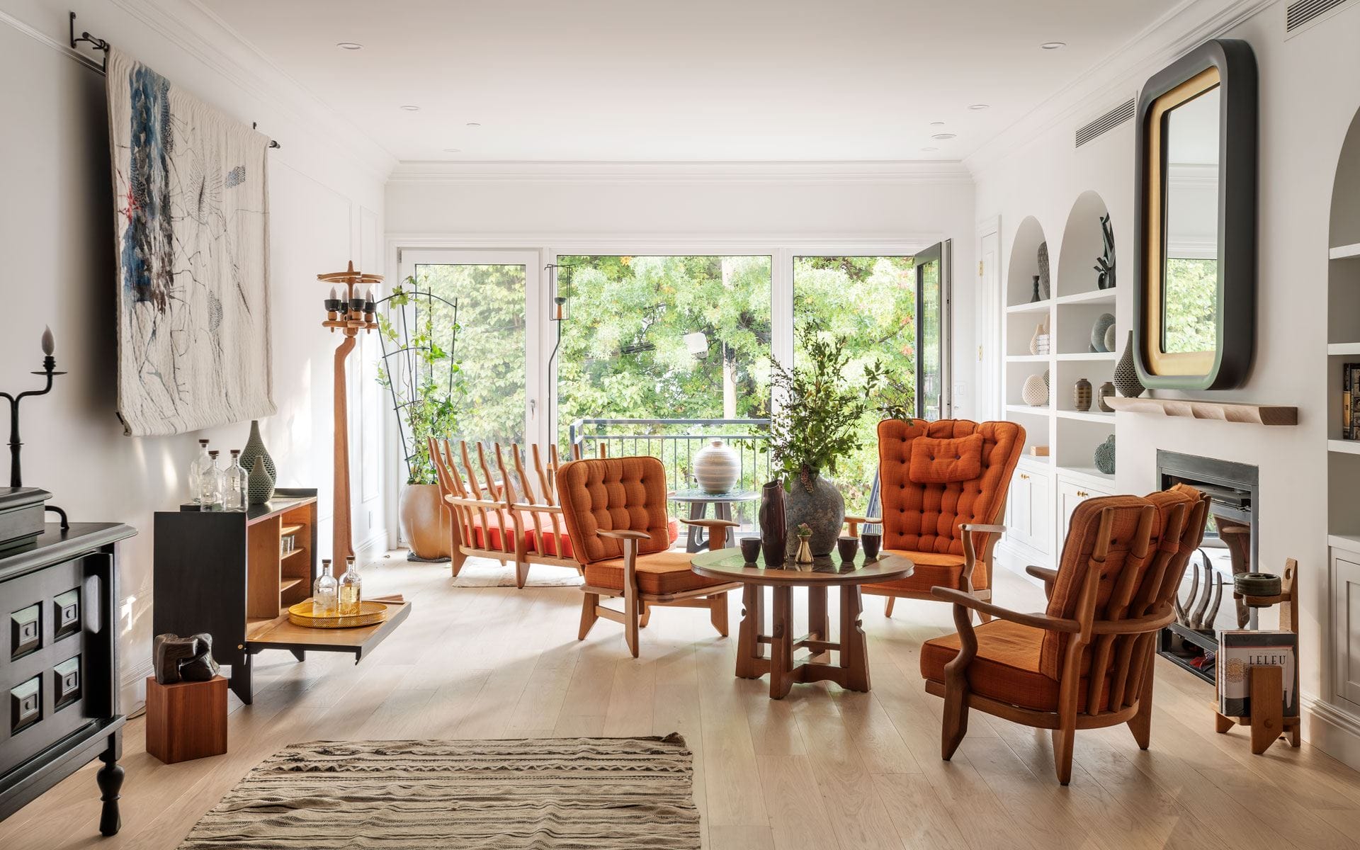 Bright living room with orange chairs, large windows, wooden floor, and green view outside. Cozy and modern interior design.