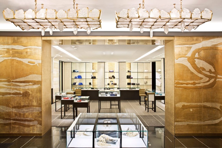 Luxury boutique interior with gold accents, glass display cases, designer handbags, and crystal chandeliers.