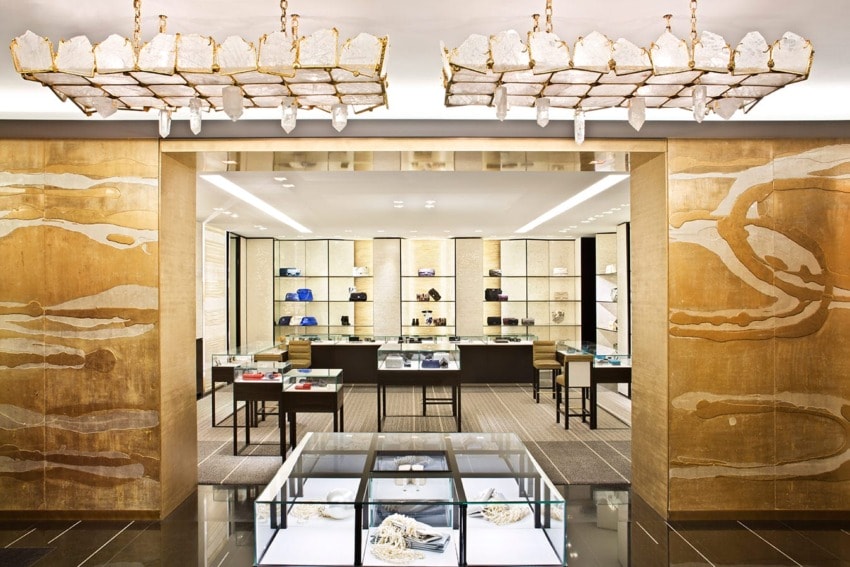 Luxury boutique interior with gold accents, glass display cases, designer handbags, and crystal chandeliers.