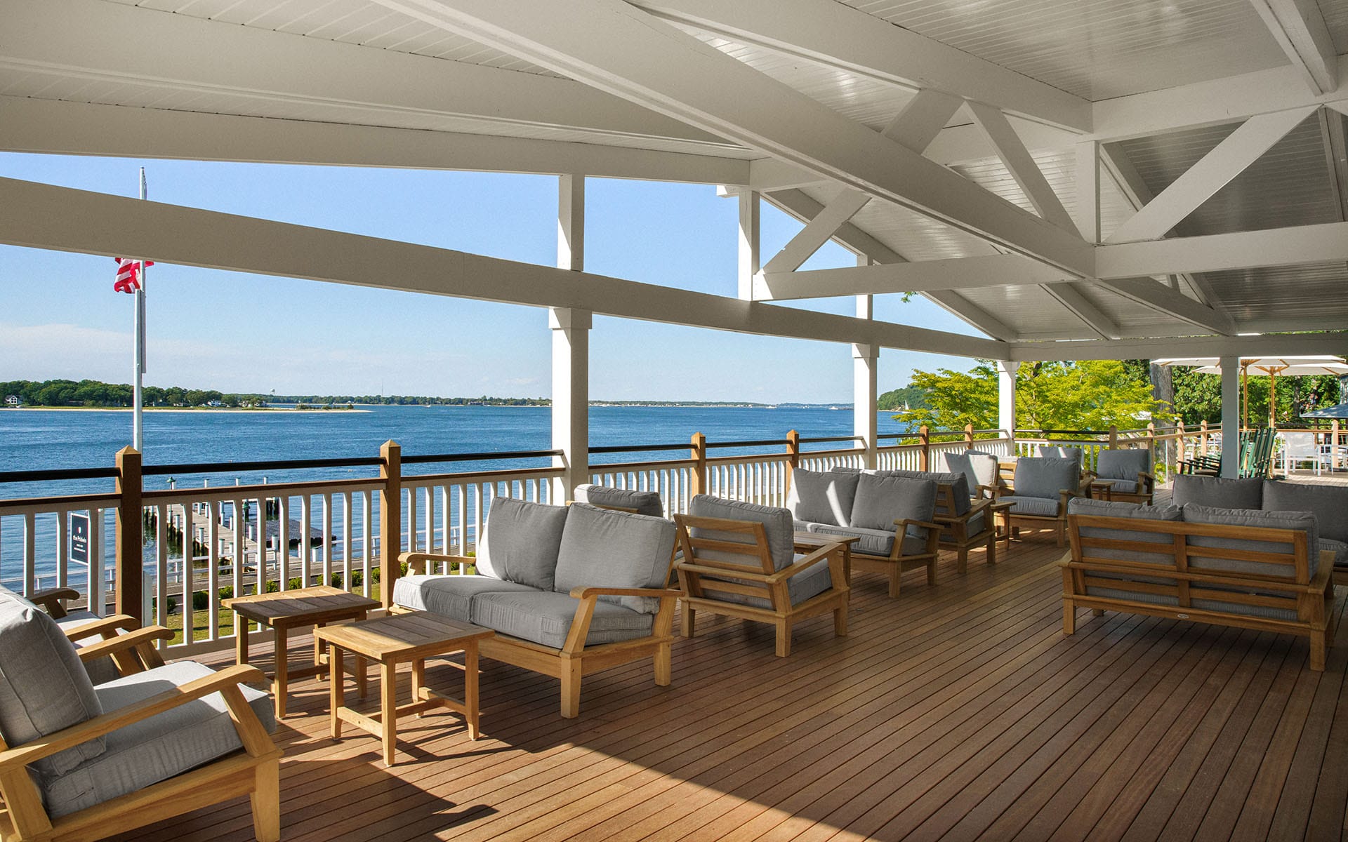 Outdoor deck with wooden furniture overlooking a scenic waterfront view under a covered structure.
