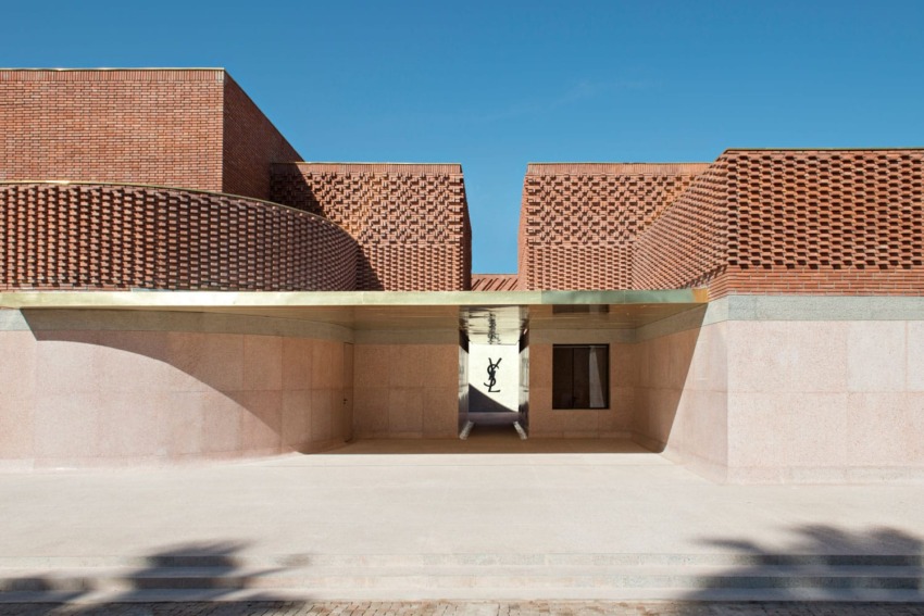 Modern architectural building with red brick facade and brass accents under a clear blue sky.
