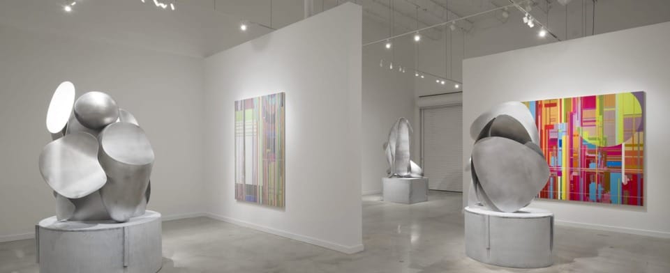 Contemporary art gallery with abstract sculptures and colorful paintings on display in a bright, modern exhibition space.