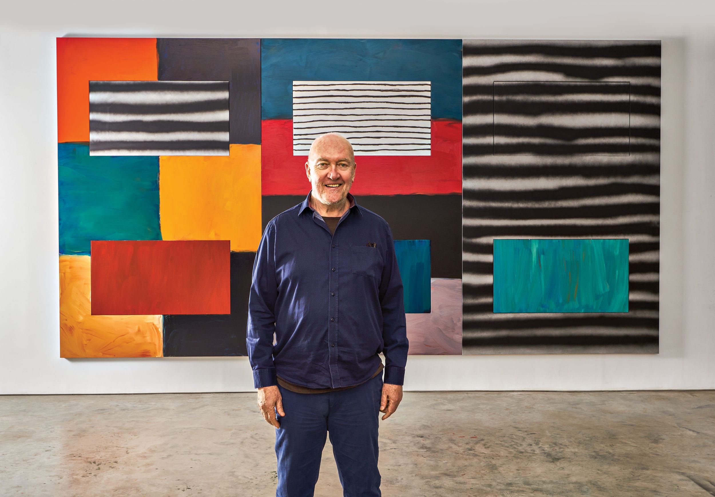 Person standing in front of a colorful abstract painting with geometric shapes and stripes in a gallery setting
