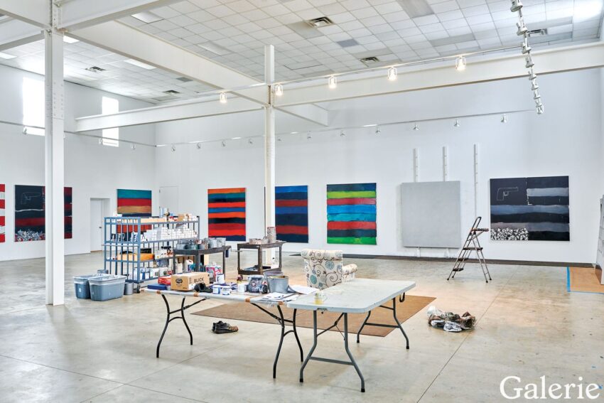 Spacious art studio with colorful abstract paintings on the walls, supplies on tables, and tall ceilings.