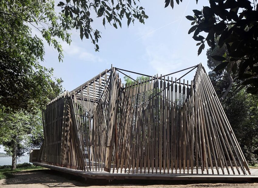 Modern geometric bamboo structure surrounded by trees under a clear sky.