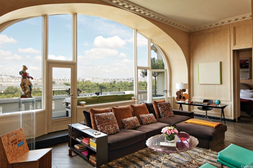 Spacious living room with large windows, cityscape view, brown sofa, decorative items, and colorful accents.