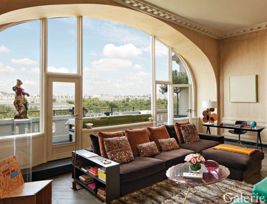 Spacious living room with large arched window, city view, modern furniture, and colorful decor elements.