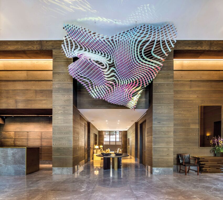 Colorful abstract ceiling installation in modern, elegant hotel lobby with wooden walls and marble floor.