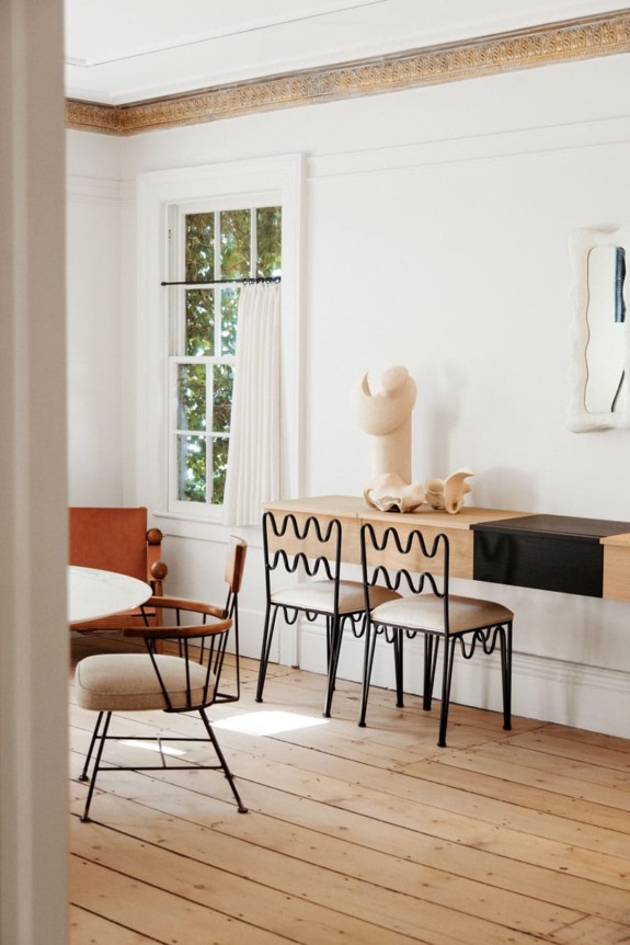 Minimalist dining room with wooden floor, modern chairs, desk, abstract sculpture, round table, and large window with curtains