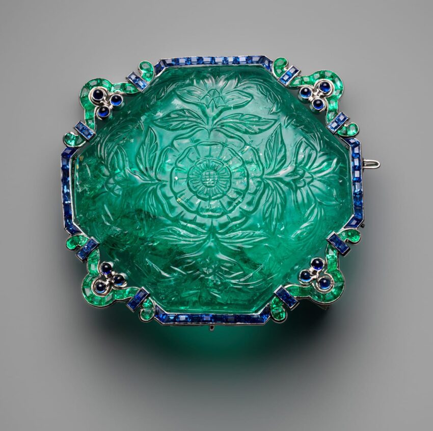 Intricately carved green floral gemstone brooch with blue and green accents on a gray background.