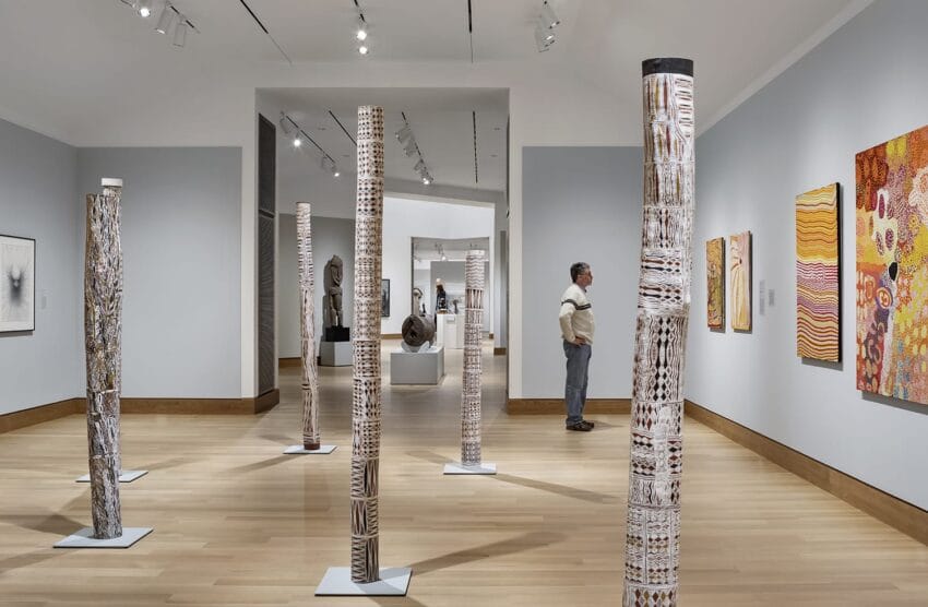 Art gallery with wooden sculptures and colorful paintings, a person observing the artwork, bright lighting highlights displays.