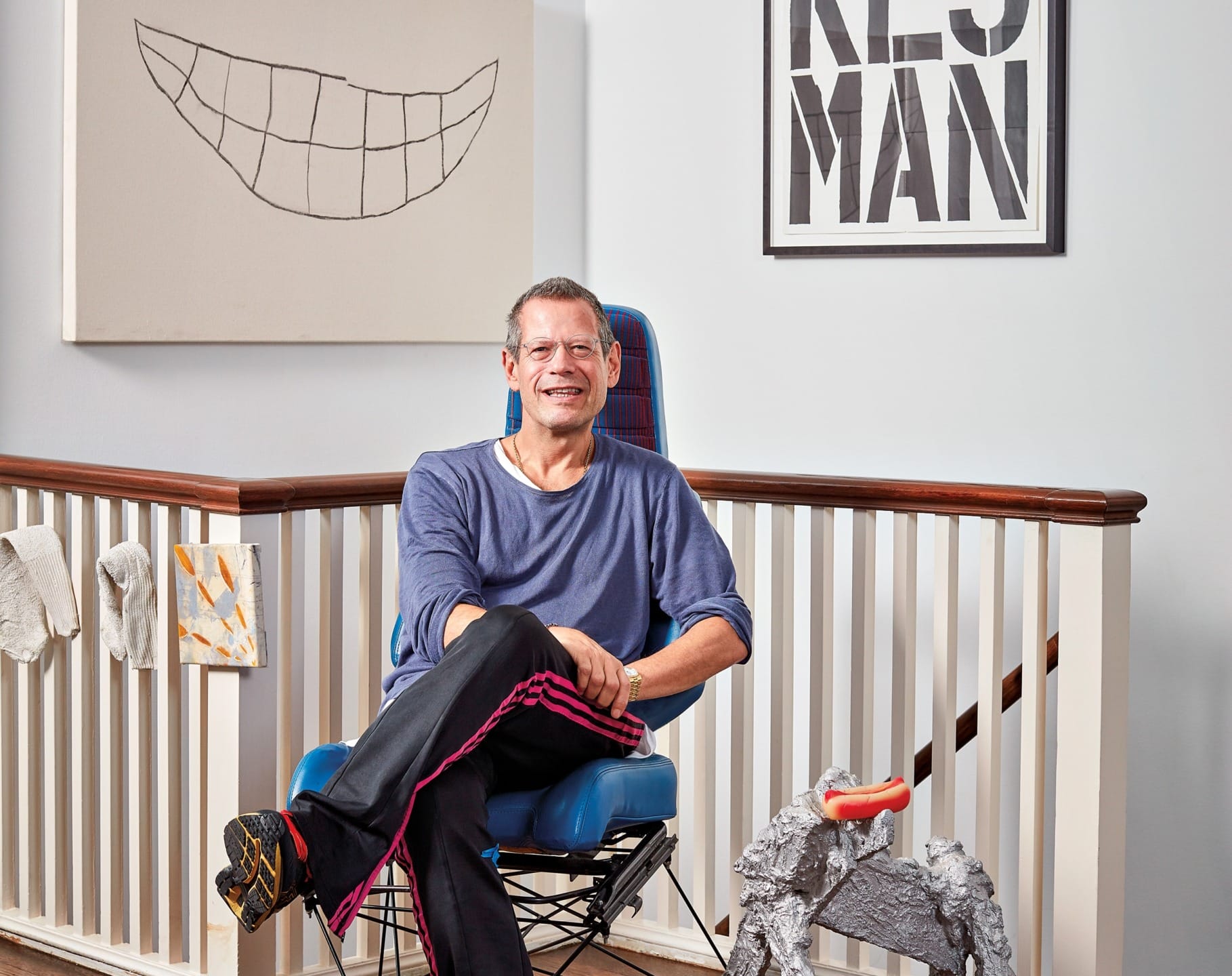 Man sitting casually in a modern art-filled room with vibrant and monochrome paintings on walls behind him.