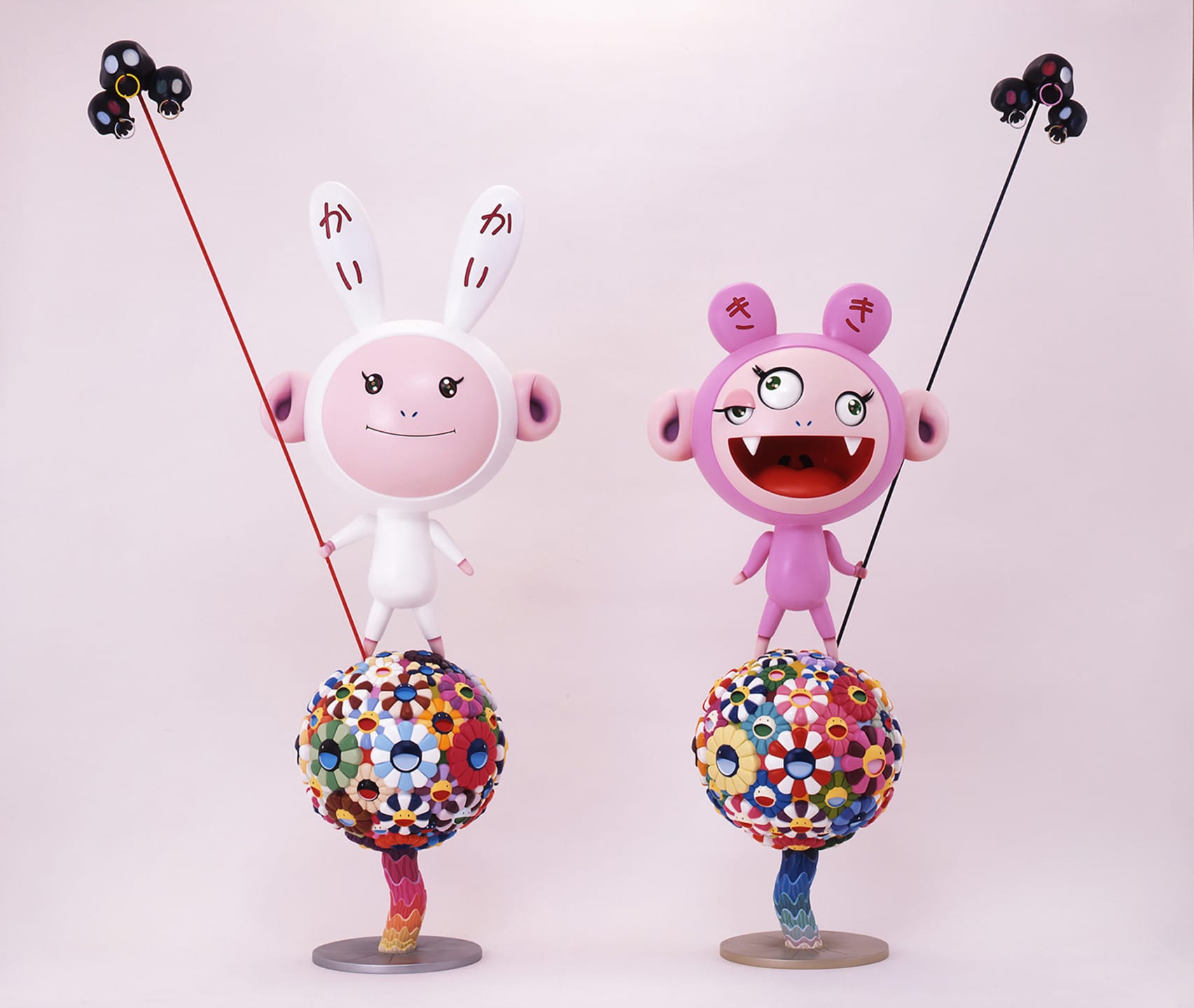 Two colorful cartoon figures standing on floral patterned spheres with playful expressions and antennas against a plain background.