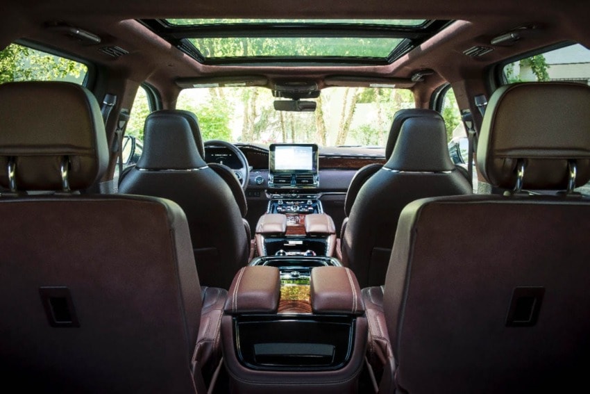Luxury car interior with leather seats, panoramic sunroof, and touchscreen display viewed from the back seats.