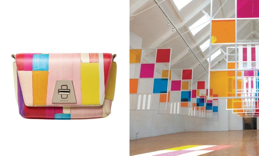 Colorful patchwork handbag next to a modern art installation with colorful suspended panels in a bright room.