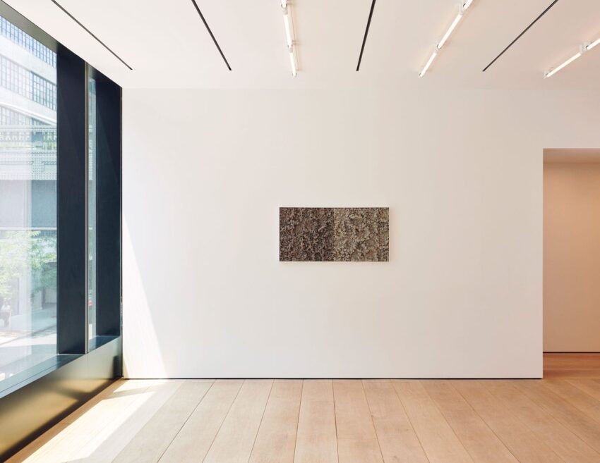 Minimalist art gallery interior with a single framed artwork on a white wall, large windows, and wooden flooring.